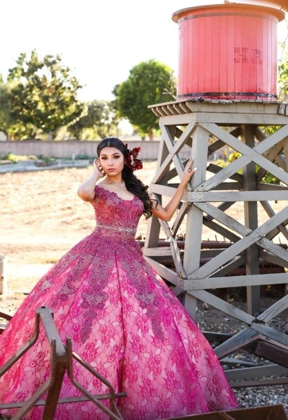 A woman in a pink Quinceanera gown standing next to a water tower