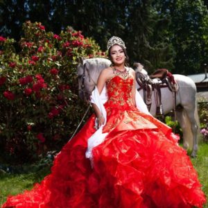 A woman in a red Quinceañera gown sitting next to a white horse