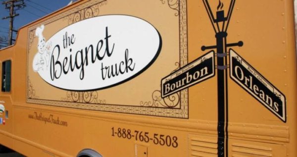 A yellow food truck parked on the side of the road, with a school bus in the background