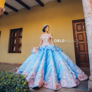 A woman in a blue and pink Quinceanera gown standing in front of a building