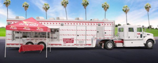 A Quinceanera themed food truck called Burger parked in a parking lot with palm trees in the background