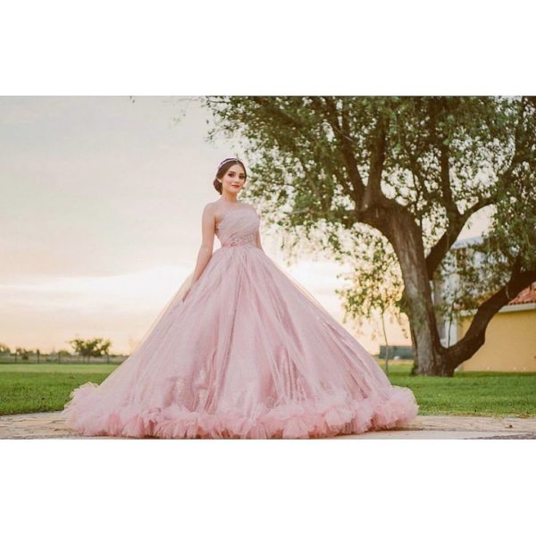 A woman in a pink Quinceanera gown standing in front of a tree