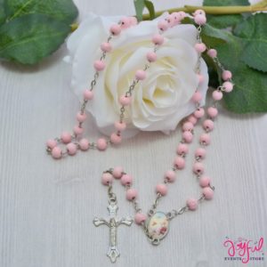 A petal necklace, a white rose, and a pink rosary on a table for a Quinceanera celebration