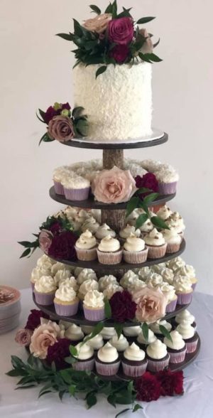Quinceanera cake and cupcake stand arrangement with a three-tiered cake, cupcakes, and flowers