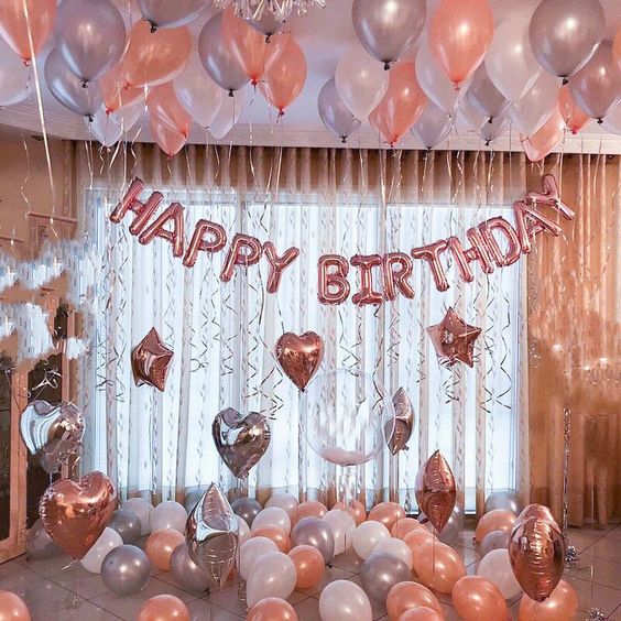 A Quinceanera celebration with a rose gold birthday party theme. The room is filled with lots of balloons and a happy birthday sign.