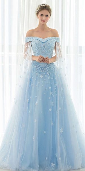 A woman in a blue Quinceañera dress standing in front of a window, showcasing the Elsa Quinceañera dress